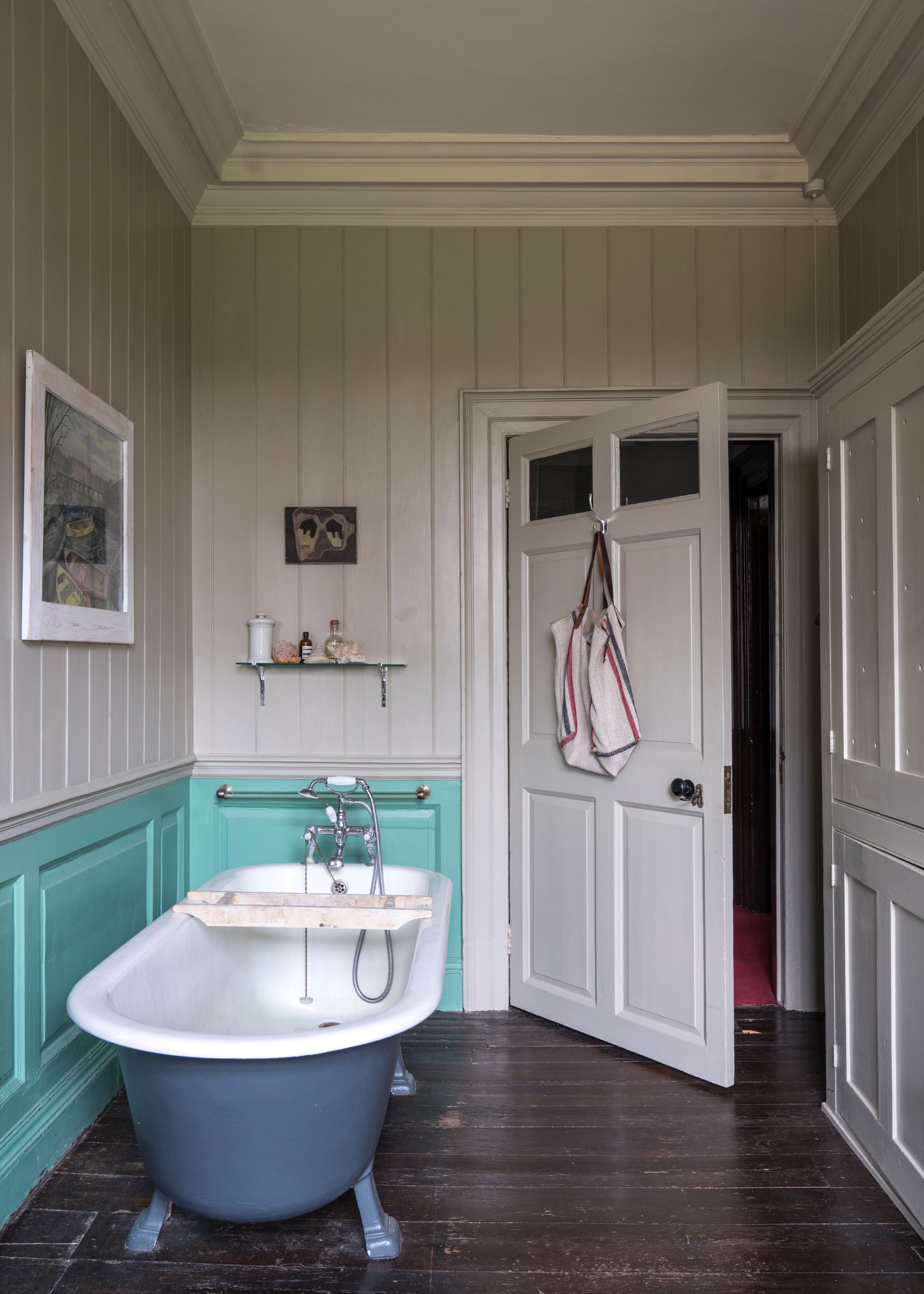 Bathroom with panelled walls painted beige, bright blue lower wall, roll-top bath, and dark wood floors.