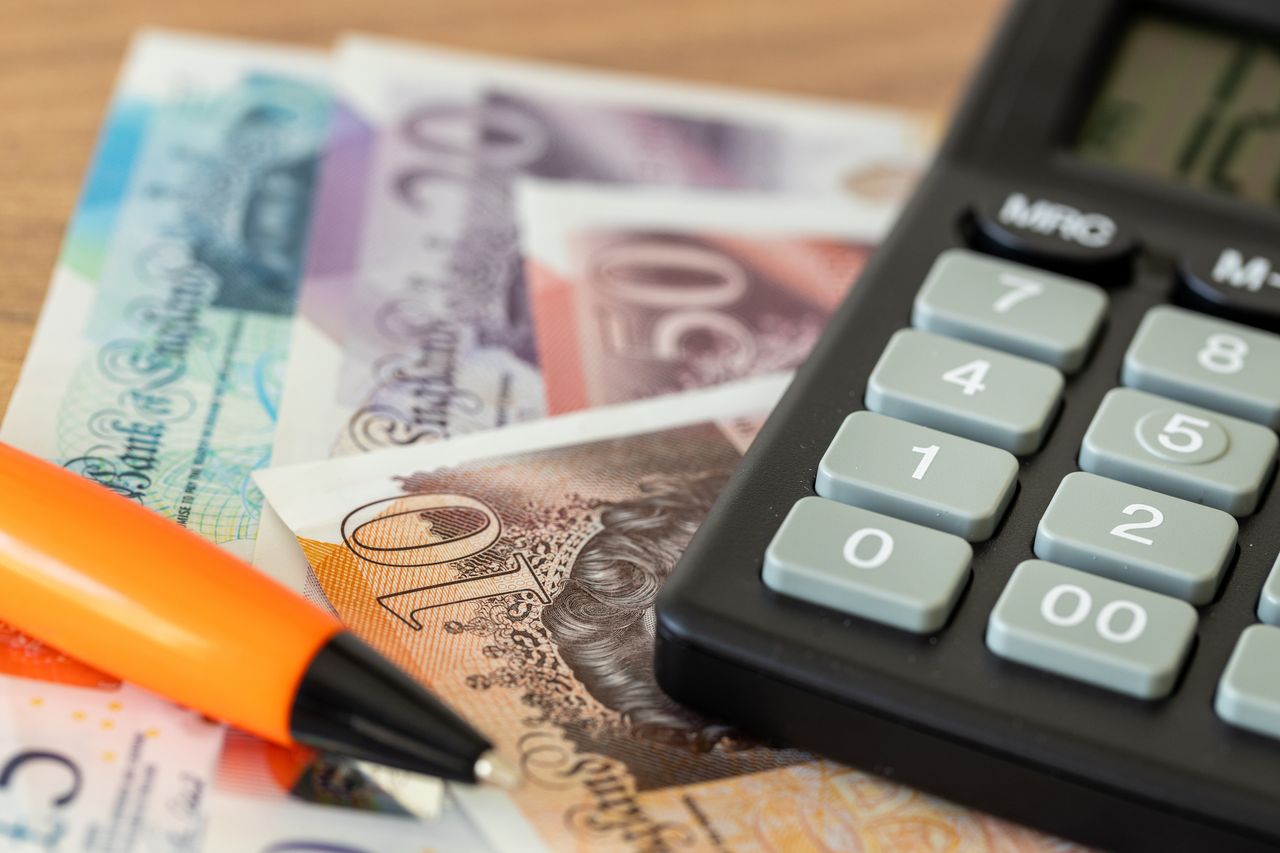 UK notes and coins sit next to a calculator on a wooden table (image: Getty Images)