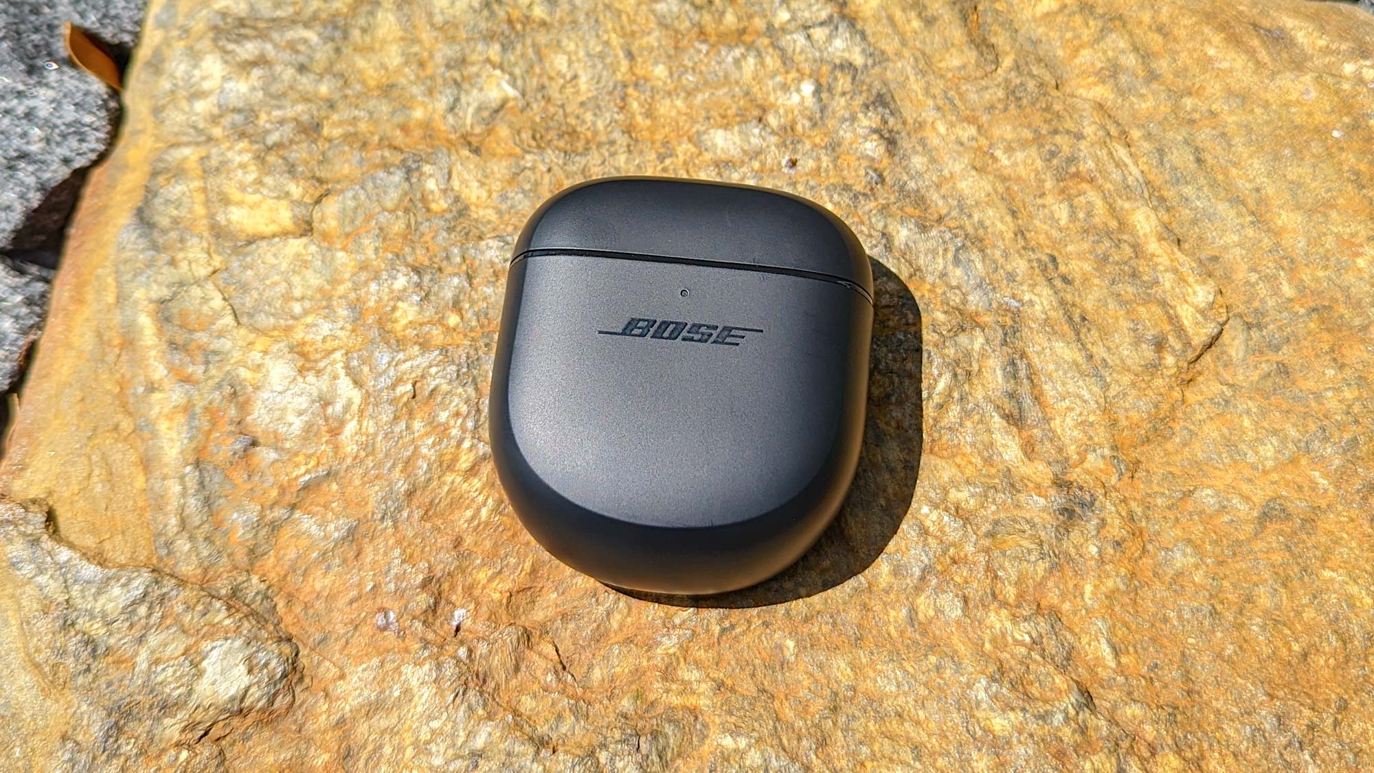 Bose QuietComfort Earbuds 2 charging case, in black on a stone surface