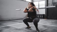 Benefits of squats: A young woman holds a barbell to her chest and performs a squat in a gym