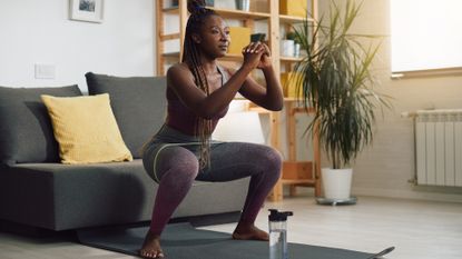 woman performing a banded squat in a living room with a short loop band around her thighs.