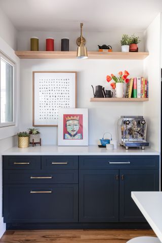 Kitchen nook with dark blue Shaker cabinets, white worktop, oak shelving and a brass wall light