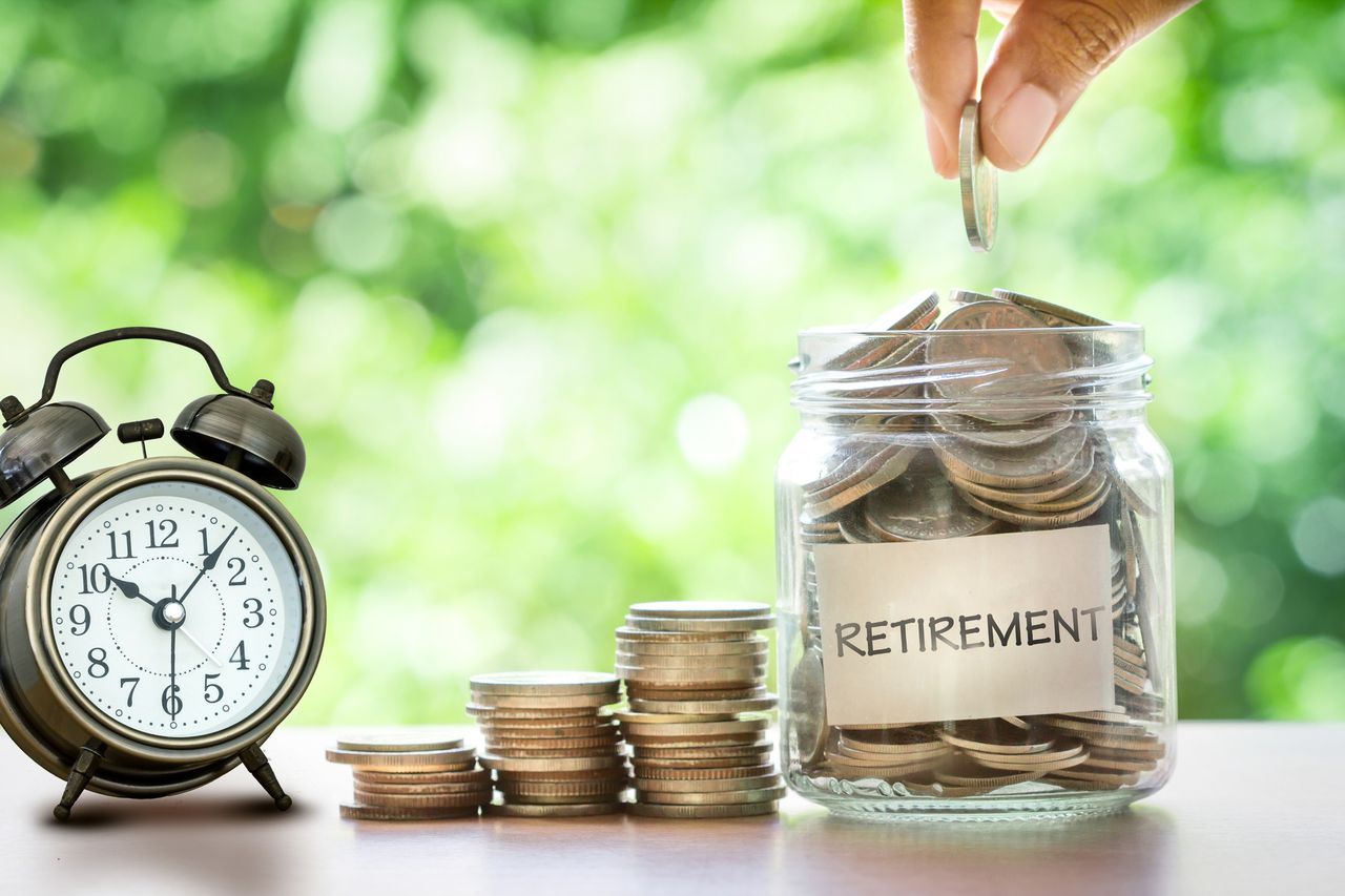 person putting a coin in a jar of coins with the word &quot;retirement&quot; on it next to a clock