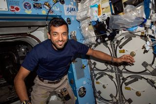astronaut floating beside lockers in space with his arm stretched out