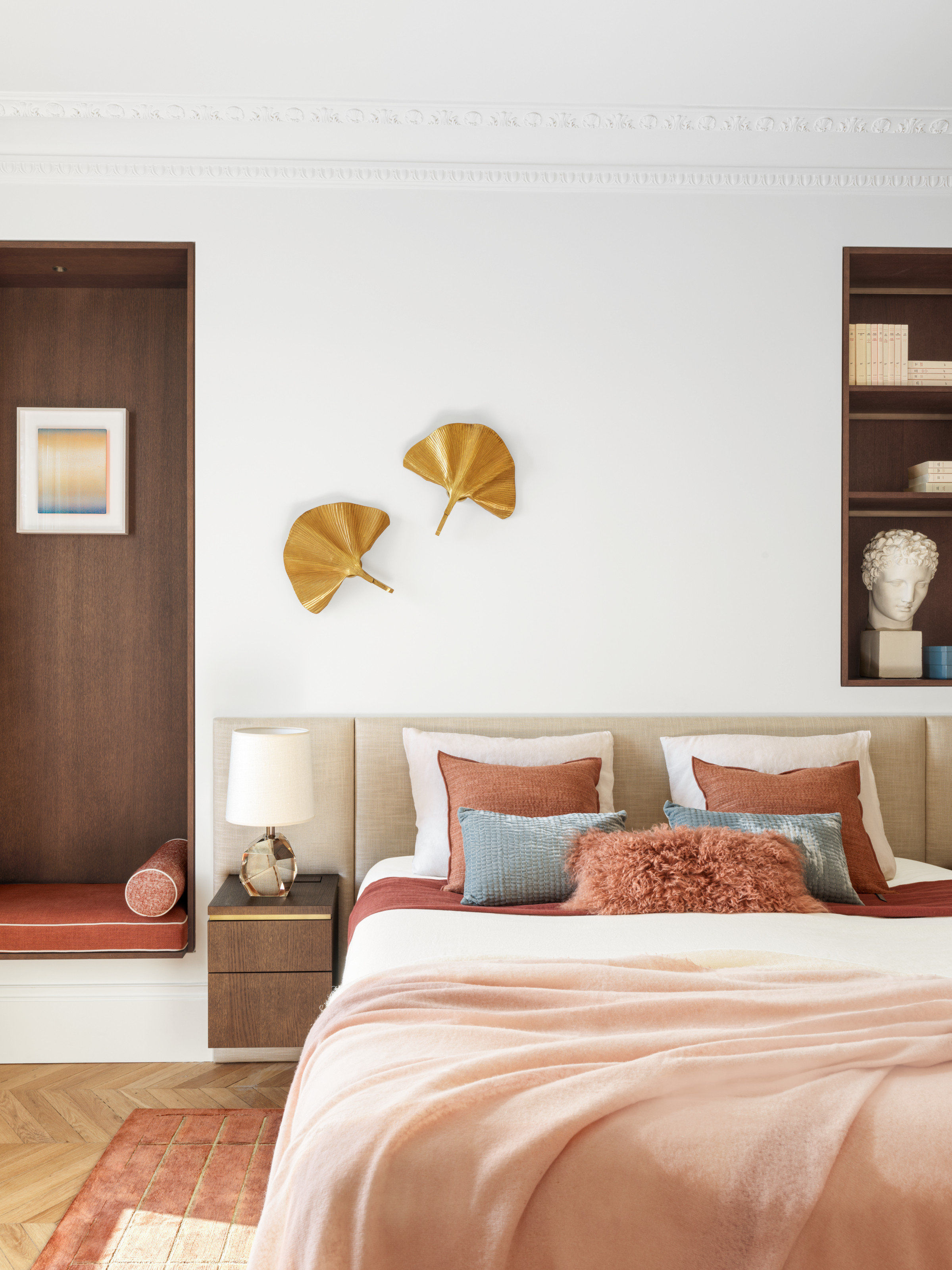 White bedroom with seating and shelving niches with dark wood panelling, beige upholstered headboard and floating wood side tables