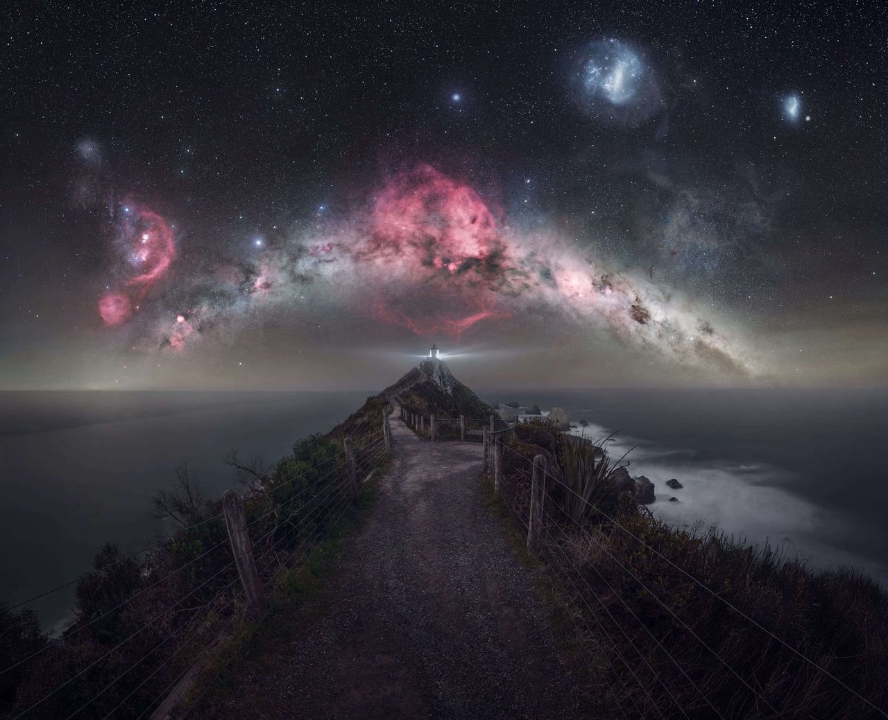 A lighthouse beams below a Milky Way clad sky.