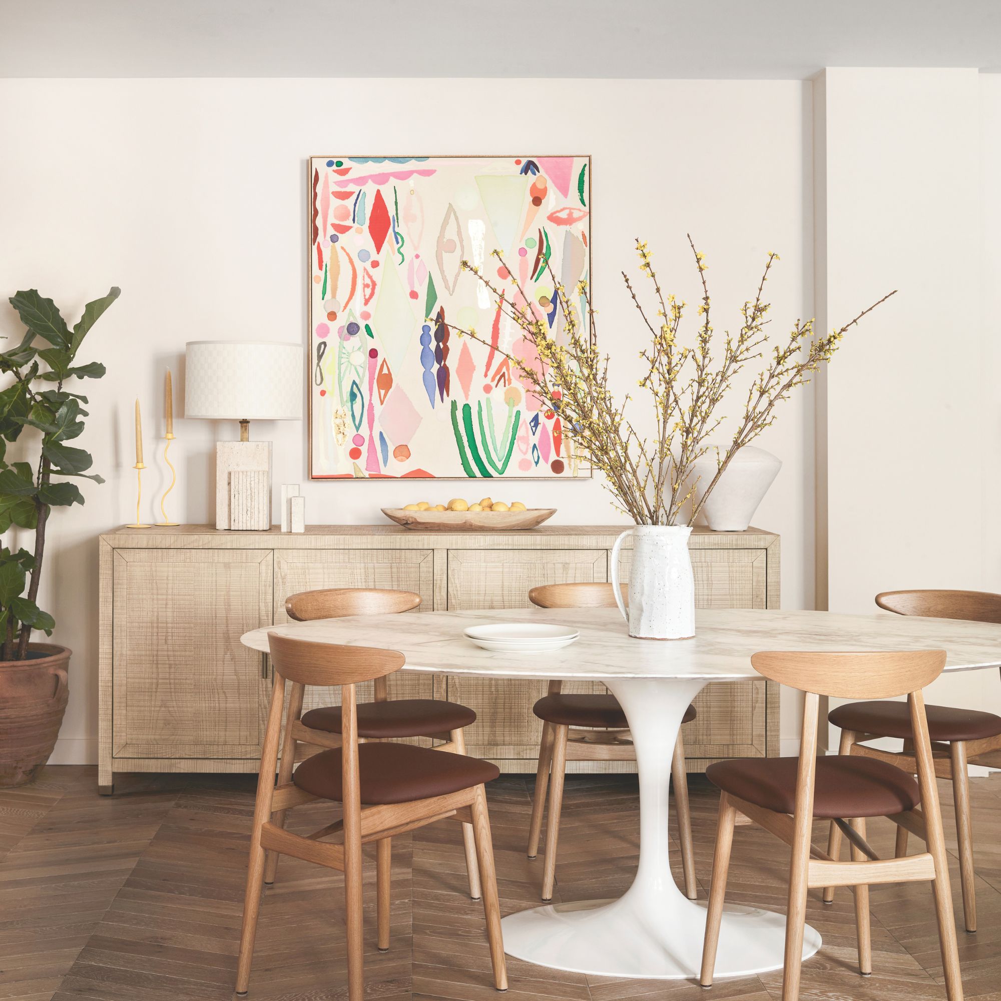 Neutral dining room with wooden floor and chairs, a marble table and a light wood sideboard with colourful artwork