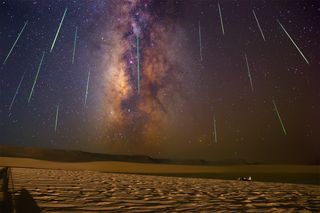Picture of the Milky Way galaxy and stars in the sky with lines of light from the Perseids meteors falling over desert sand at night