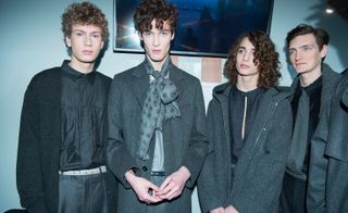 Four male models wearing wearing suits and trousers in shades of blue and black, raglan-sleeved trenches, complete with exaggerated epaulets, which were teamed back with Shetland wool crew neck sweaters and loosely cut trousers, finished with pussy-bow tied fringed scarves.