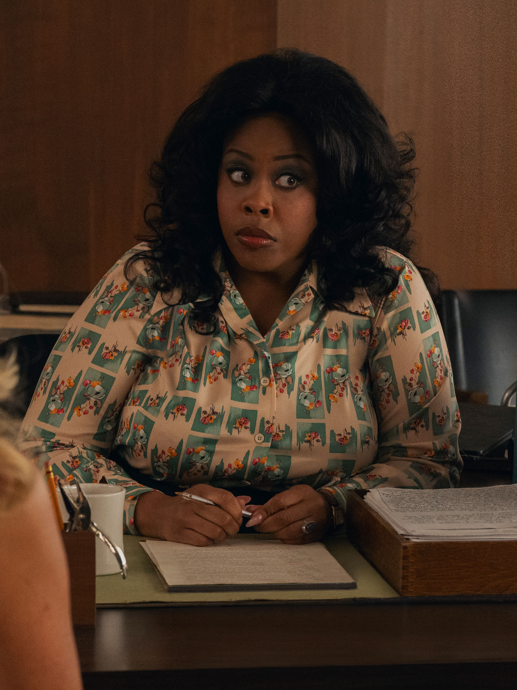 Amber Chardae Robinson is pictured wearing a Palm Royale season 2 outfit featuring a &#039;60s printed shirt