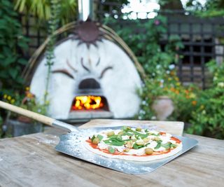 An outdoor pizza oven with a pizza on a paddle at the front