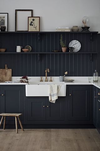 A matte black tongue and groove kitchen with bright white worktop and butler sink