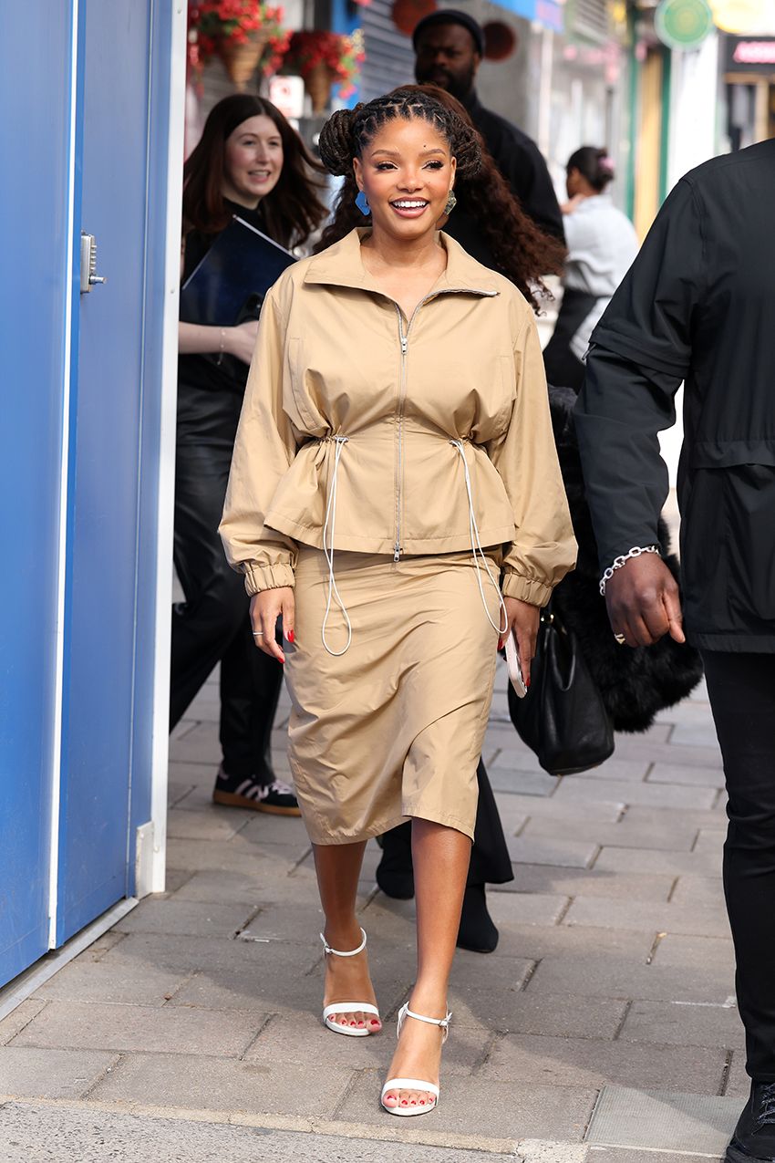 Halle Bailey wearing a tan jacket and matching skirt with white heel sandals