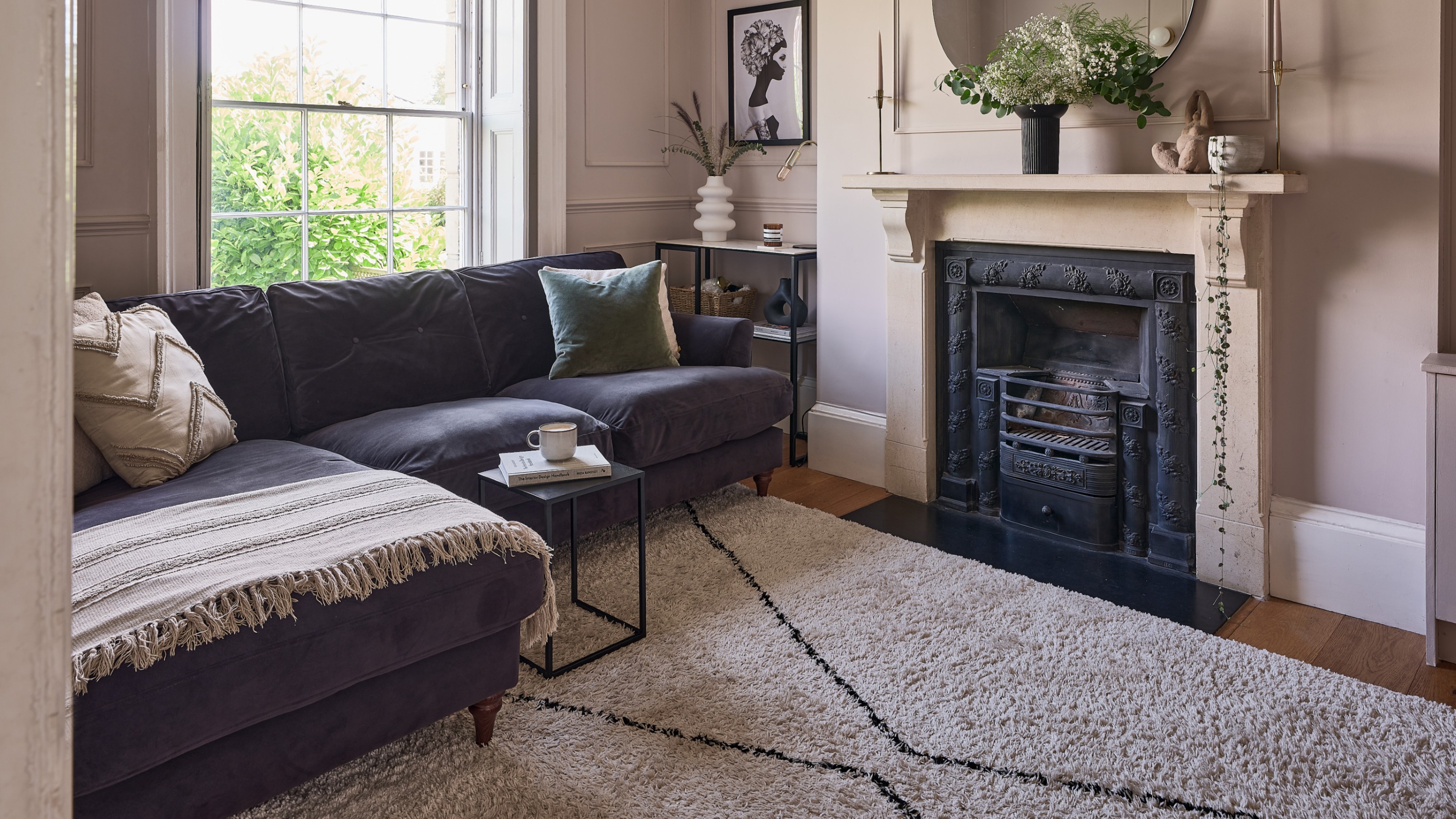 A pink-painted living room with a dark blue velvet chaise sofa and a Berber-style rug
