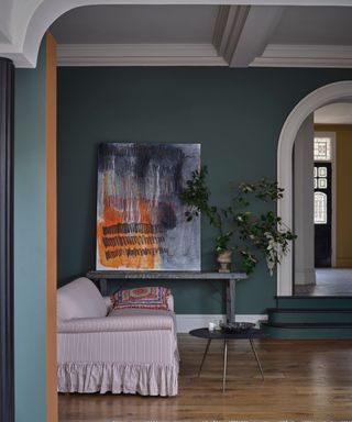 living space with dark green walls, white trim and ceiling, bold artwork, light pink striped sofa and wood floors