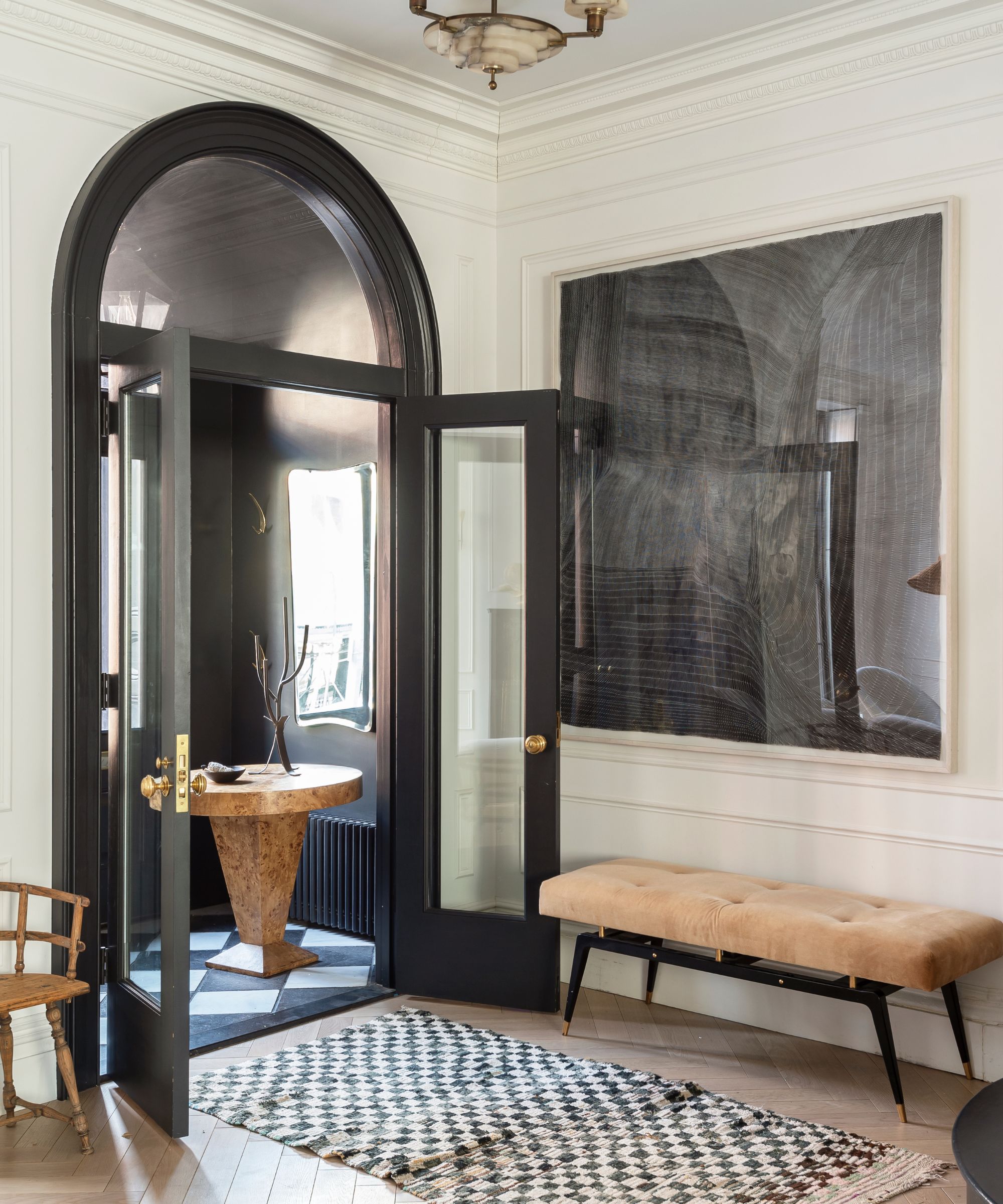 Transitional style hallway with checkered rug, velvet bench, curved doorway, burl wood table and large painting