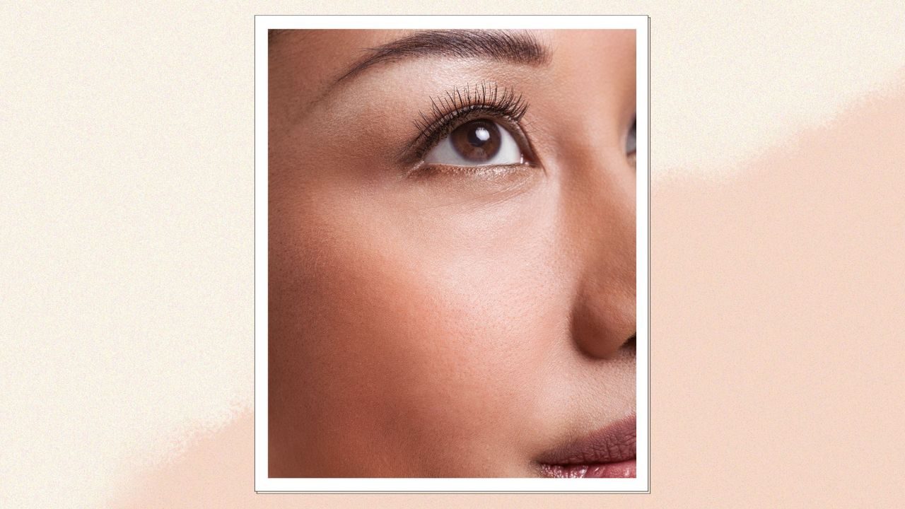 A close up shot of a woman looking upward with eyelash extensions on a peach and cream backdrop