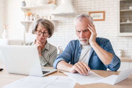 Depressed sad concentrated senior old elderly couple dealing with documents, solving financial problems, feeling confused while receiving mortgage loan contract at home kitchen