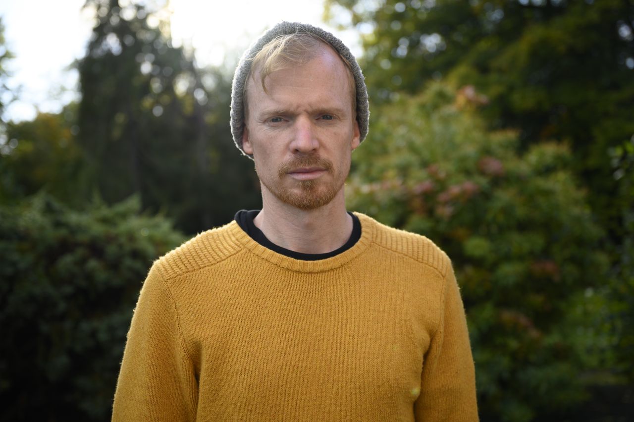 A man in a yellow jumper and hat standing in a garden