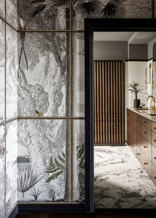 The entryway to a bathroom with his and hers sinks and wood, gold and marble accents