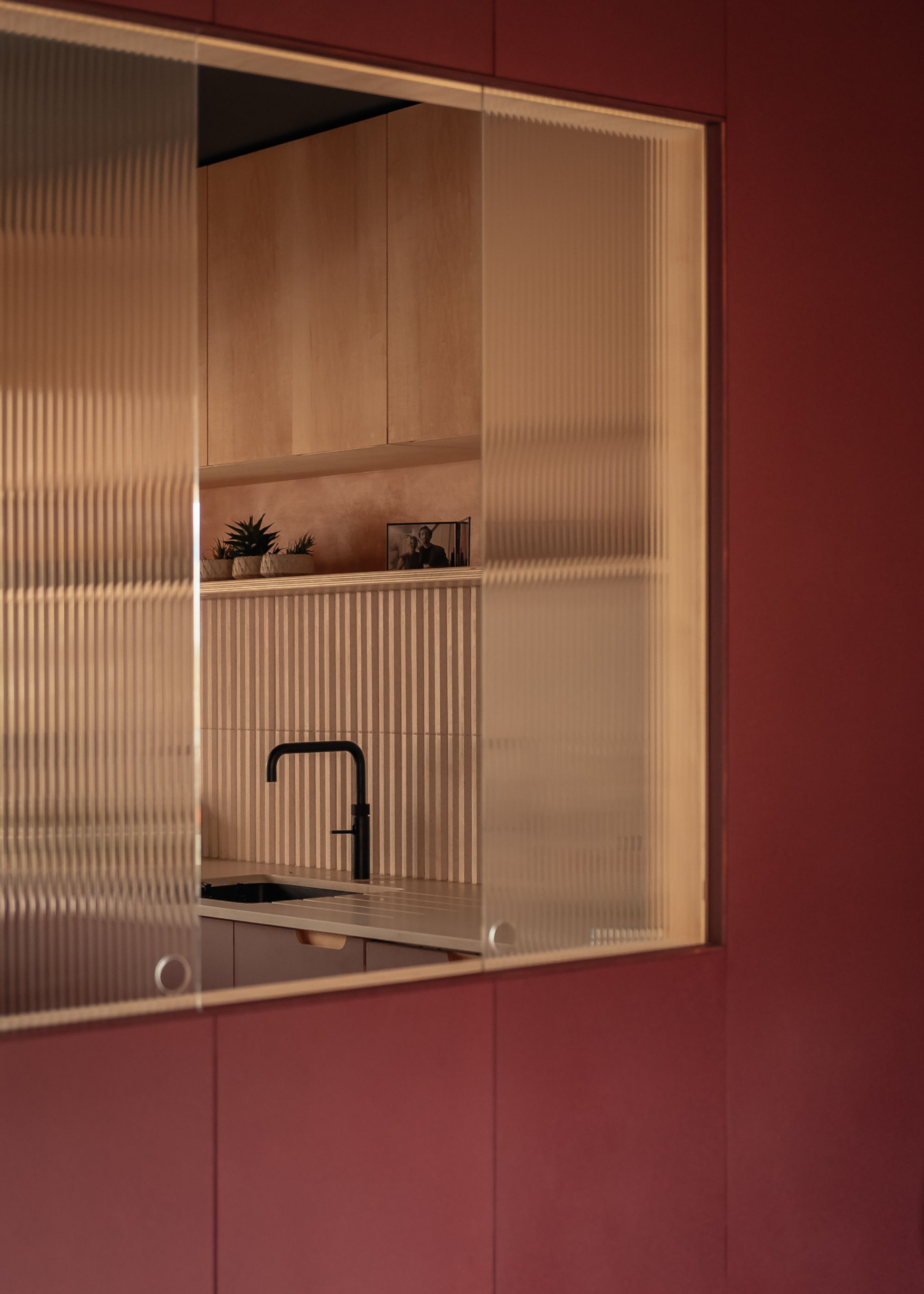 A kitchen painted red, with a hatch in reeded glass
