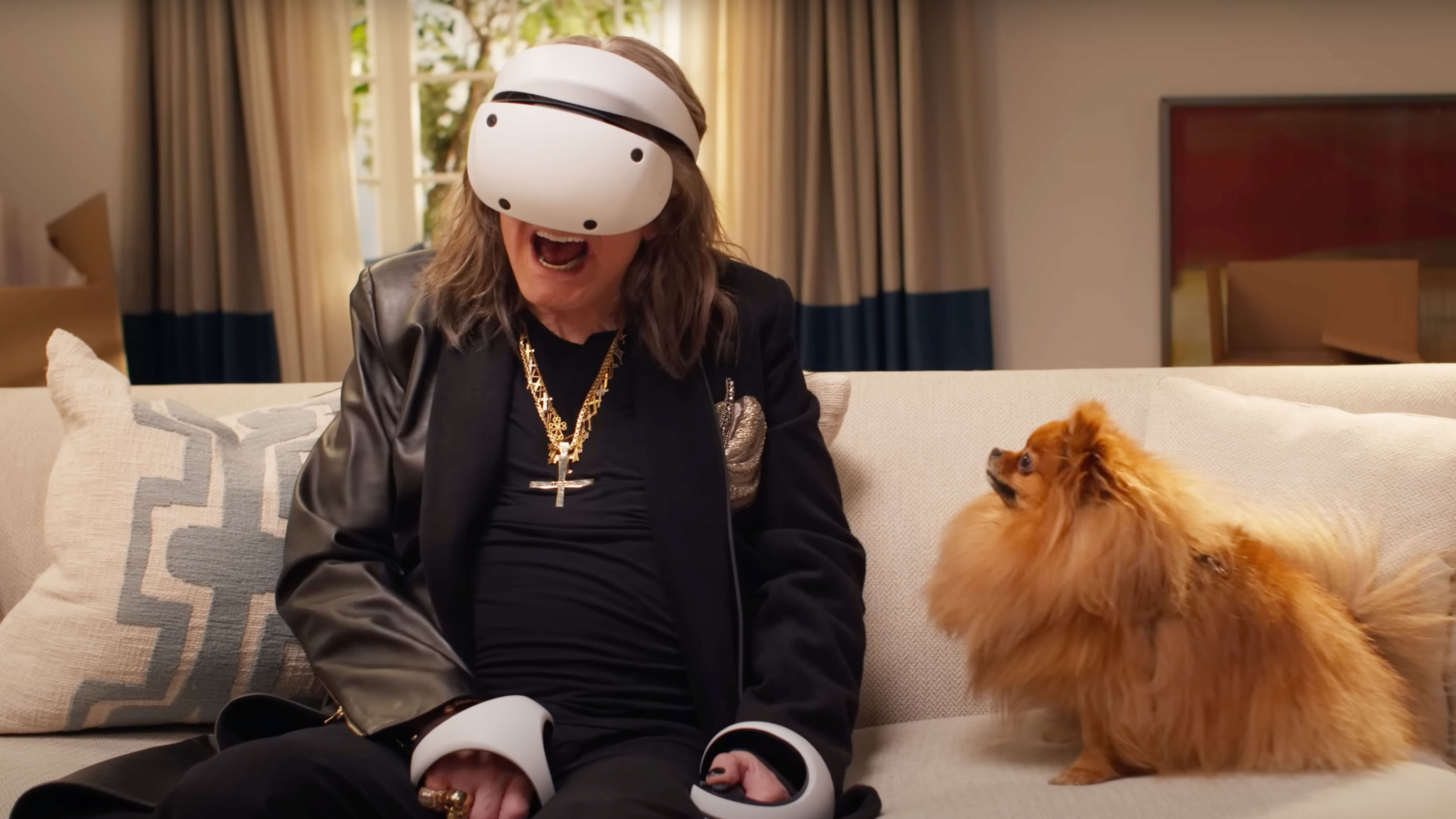 A shot of Ozzy Osbourne wearing the PSVR 2 headset whilst sat on a sofa with a dog looking at him