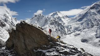 A mountainous landscape photo of two climbers climbing a peak