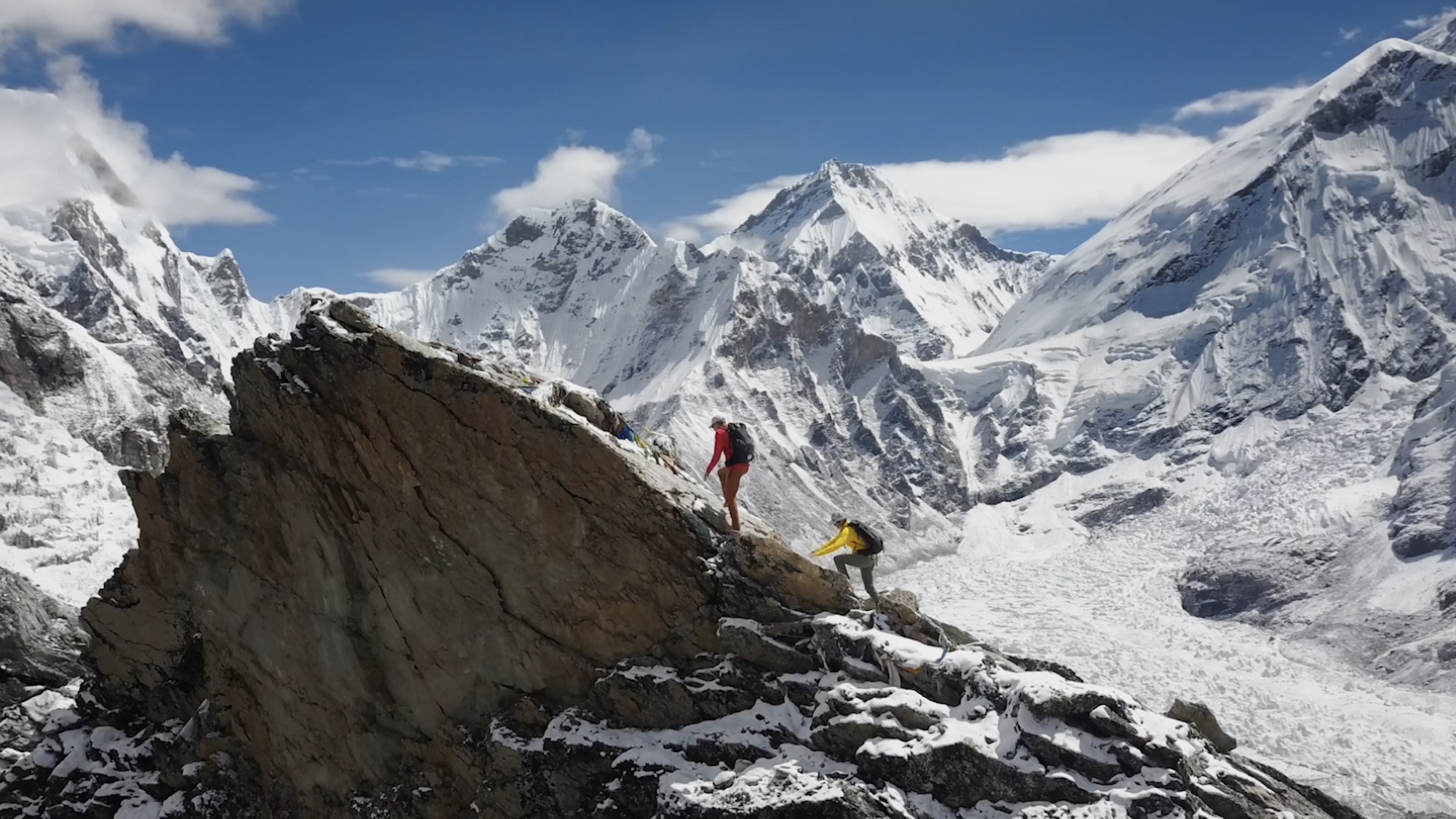 A mountainous landscape photo of two climbers climbing a peak