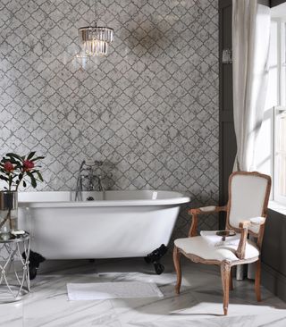 a grand bathroom with a freestanding roll top, ornate tiles and grand armchair
