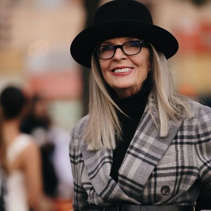 Diane Keaton wearing a hat, glasses, check blazer with a medium length hair style