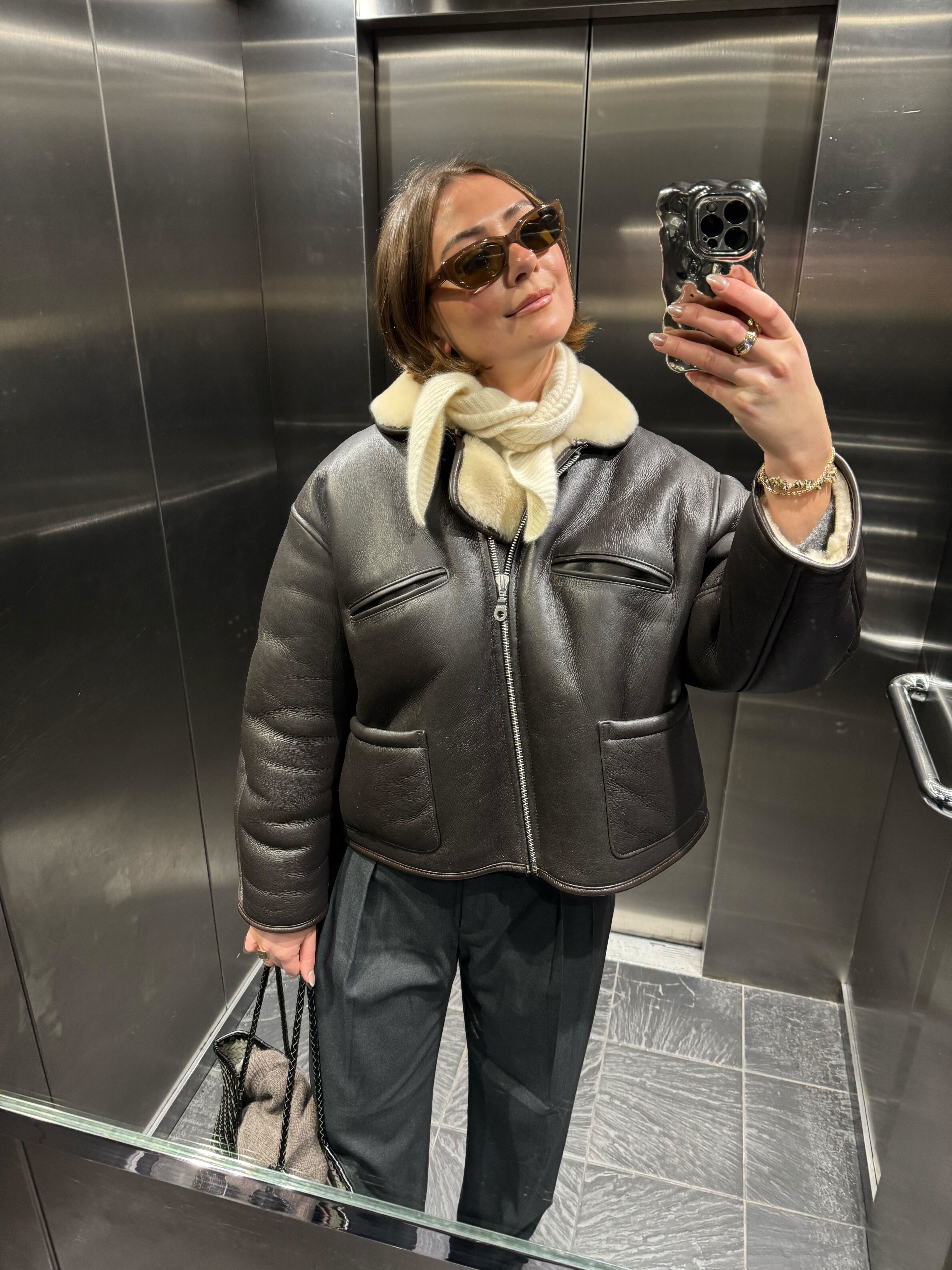 Who What Wear Acting Fashion Editor @sophie_robyn wearing a brown sheepskin leather jacket with grey trousers.