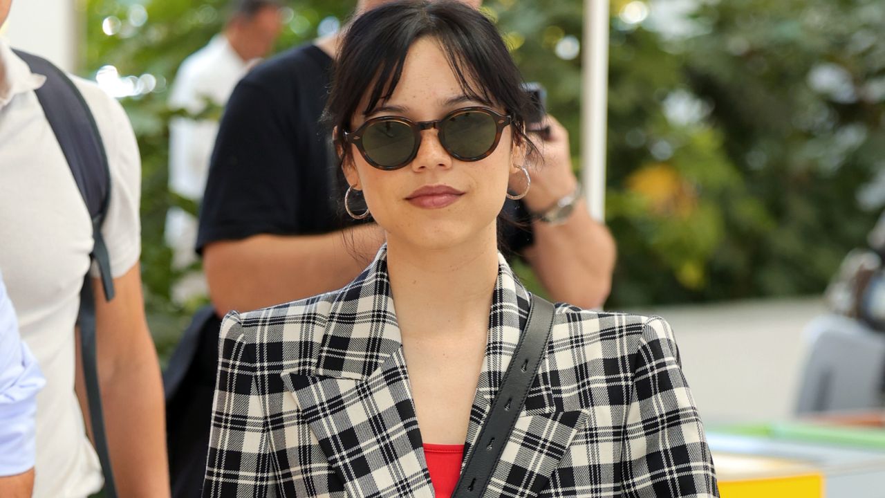 Jenna Ortega wearing a plaid blazer, a red top, and sunglasses 