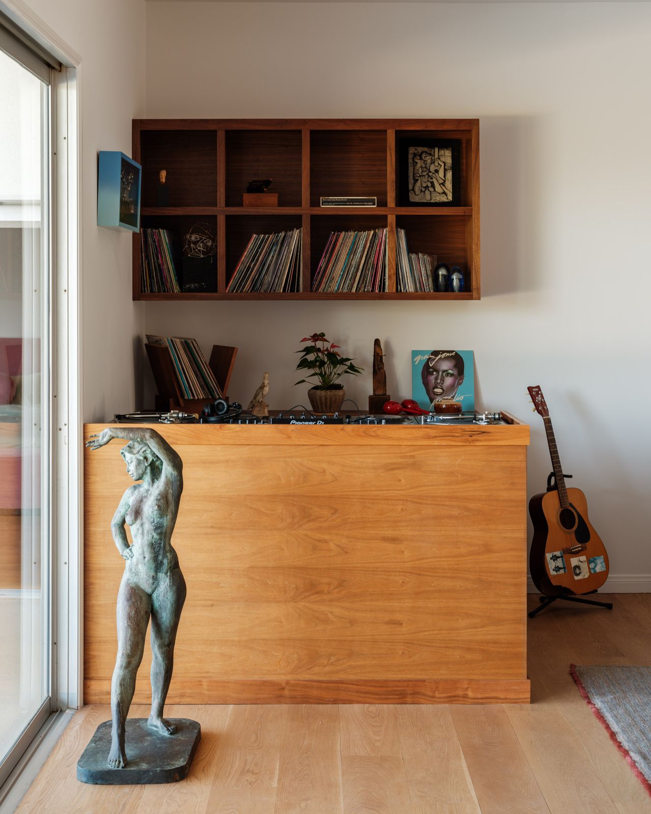 Image of a vinyl bar in the corner of a white living room. There is a large wooden DJ bar with a statue in front of it and a floating shelf on the wall behind it.