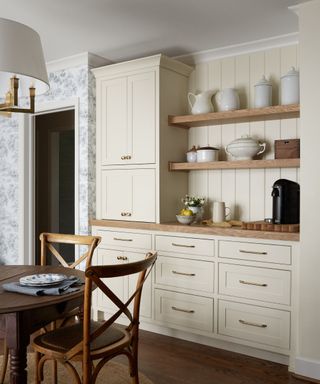 An off-white coffee nook with brass hardware and wooden open shelving displaying a ceramics collection