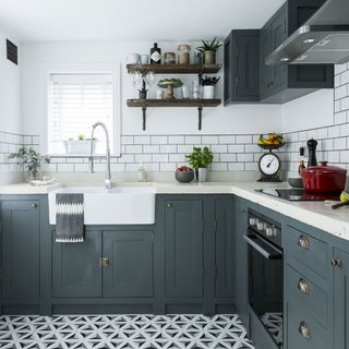 kitchen with dark grey cupboards with white marble top, white brick wall tiles, grey, black and white triangular pattern flooring and industrial wooden open shelves on the wall
