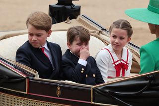 Prince Louis, alongside Prince George and Princess Charlotte, holds his nose as he rides in the carriage procession at Trooping the Colour