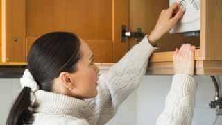 woman adjusting dials on boiler that is housed in a wall mounted cupboard