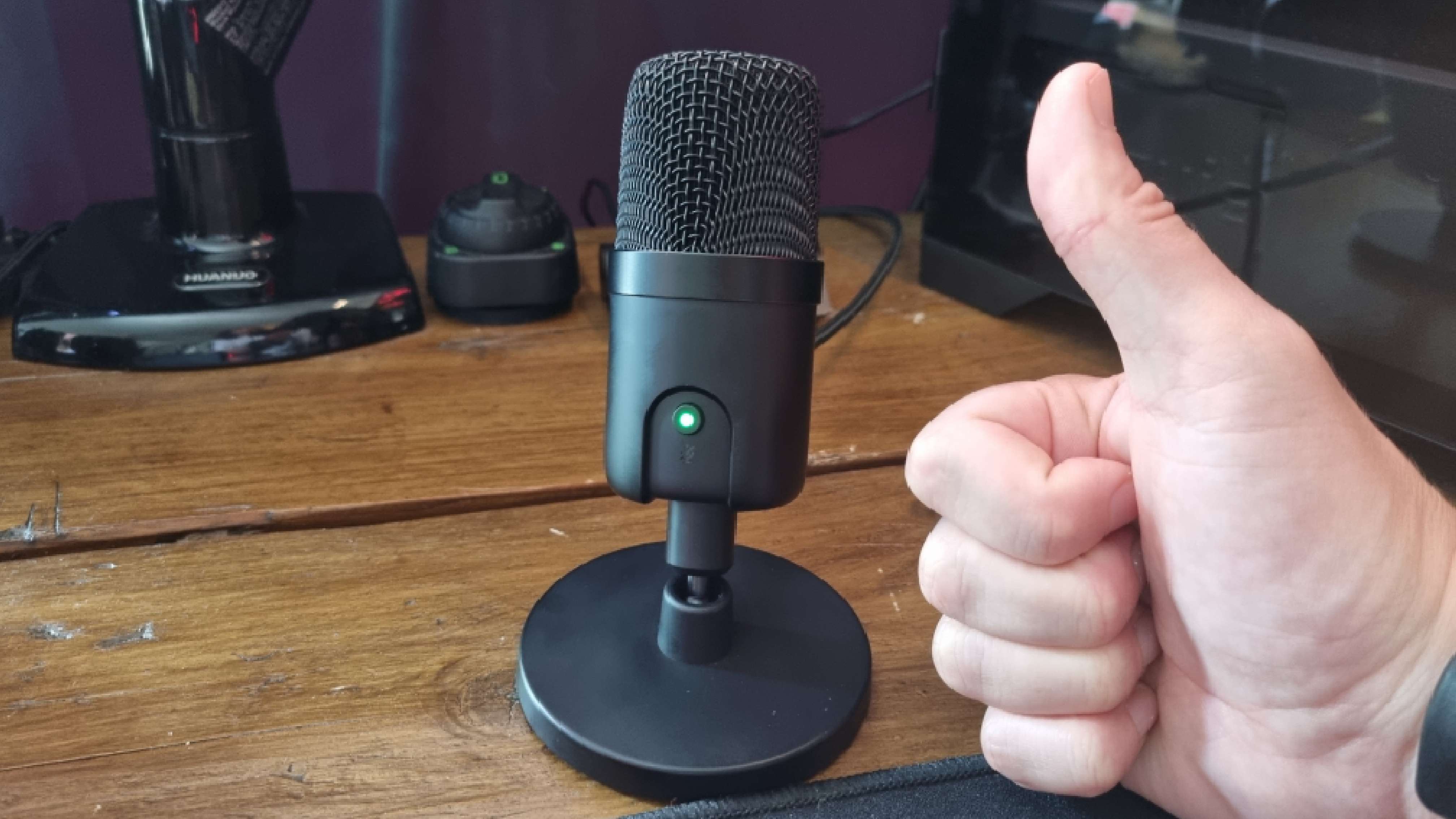 An Amazon Basics USB Condenser Microphone on a desk, with a hand giving the big thumbs up