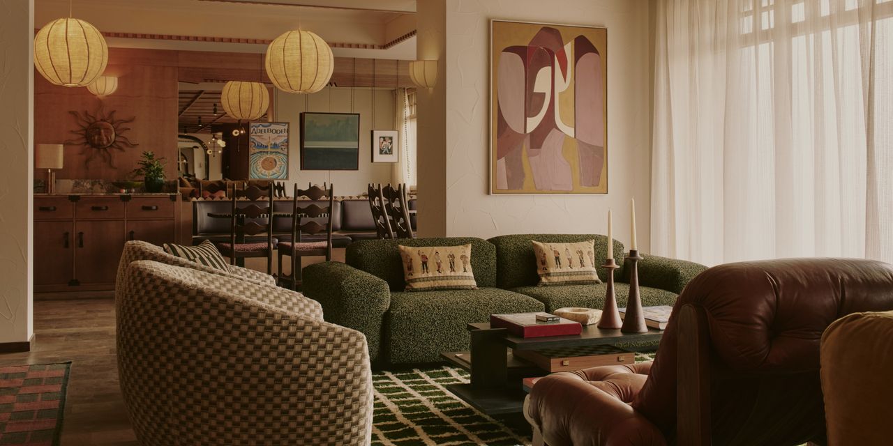 A 1970s-inspired hotel lounge features an array of voluminous seating, including a green shearling sofa and leather armchairs, colorful wall art, pendant paper lanterns, and multiple striking rugs.