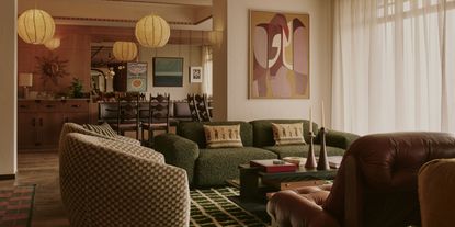 A 1970s-inspired hotel lounge features an array of voluminous seating, including a green shearling sofa and leather armchairs, colorful wall art, pendant paper lanterns, and multiple striking rugs.