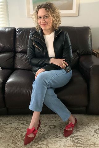 The author modelling a leather jacket, white top, blue jeans and red shoes.