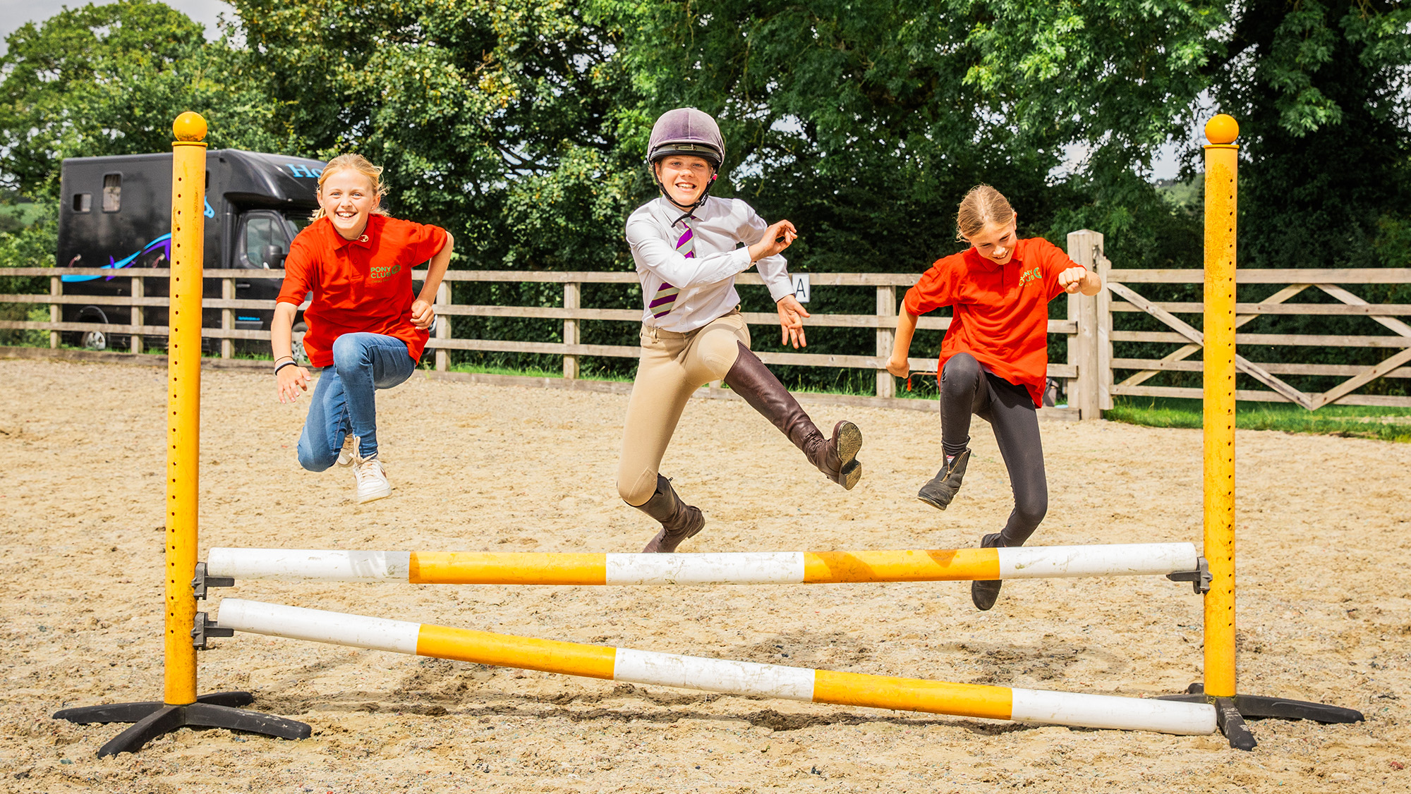 Three Pony Club members at Pony Club camp jumping over a showjumping fence on foot