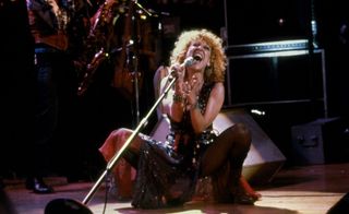 Bette Midler sings will squatting and holding a microphone in 'The Rose'