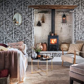 cosy living room or snug with lit wood burner in a white painted alcove, armchairs and sofa with cushions and fabric throws