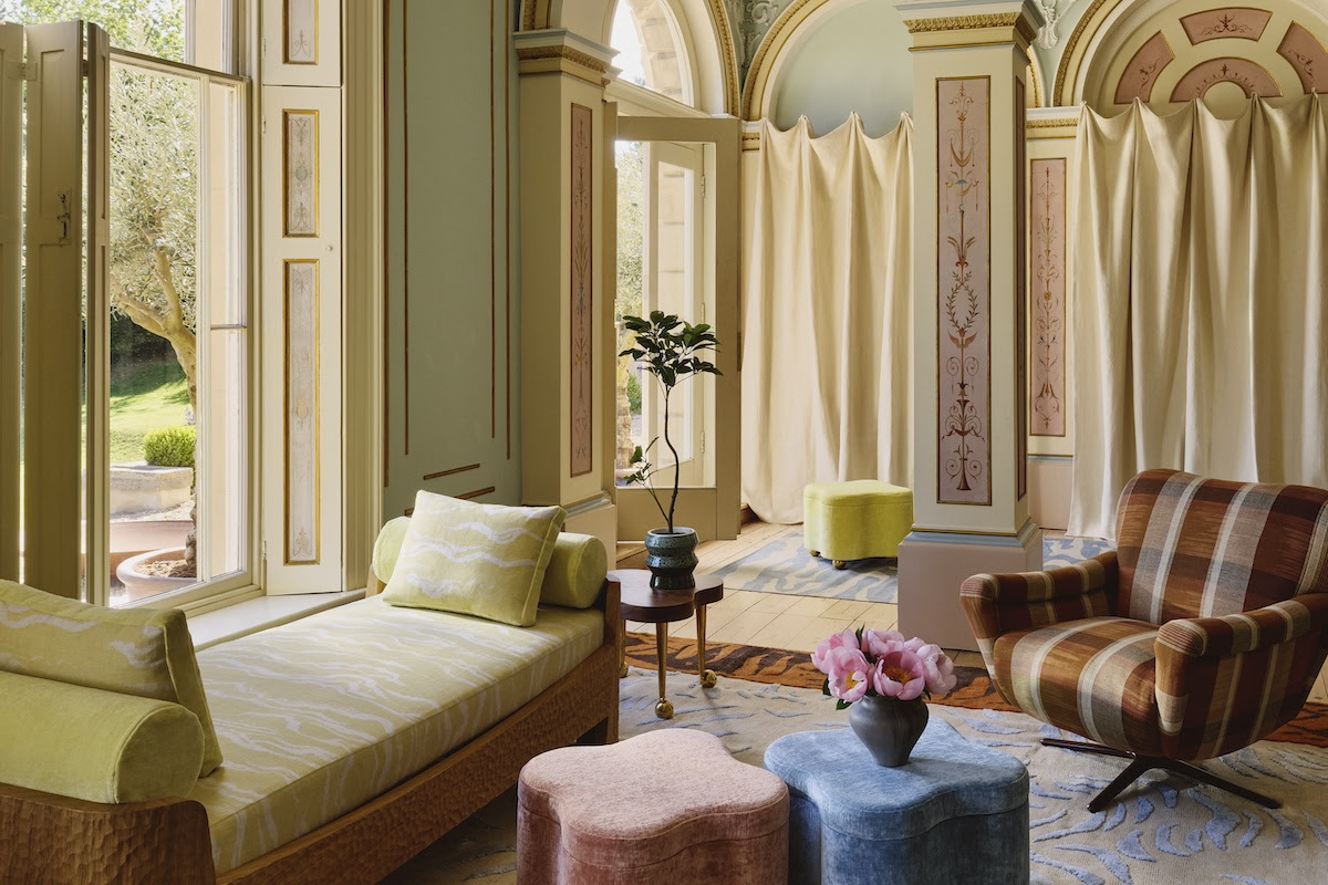 Image of a traditional, large living room with a pastel color palette. There are hand-painted details on the wall and patterned upholstery across the room.