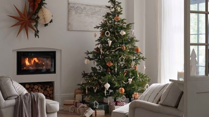 A real Christmas Tree in the corner of a white living room decorated with paper baubles