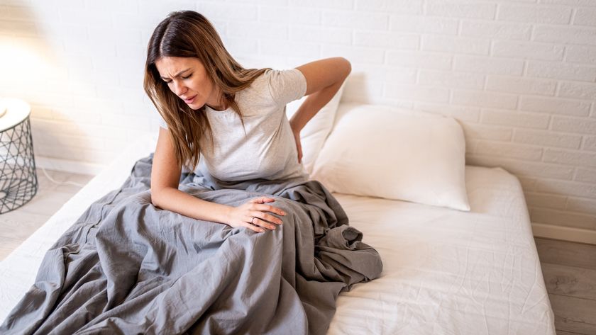 A woman with long dark hair holds her back which is sore after sleeping on a mattress that&#039;s too firm for her