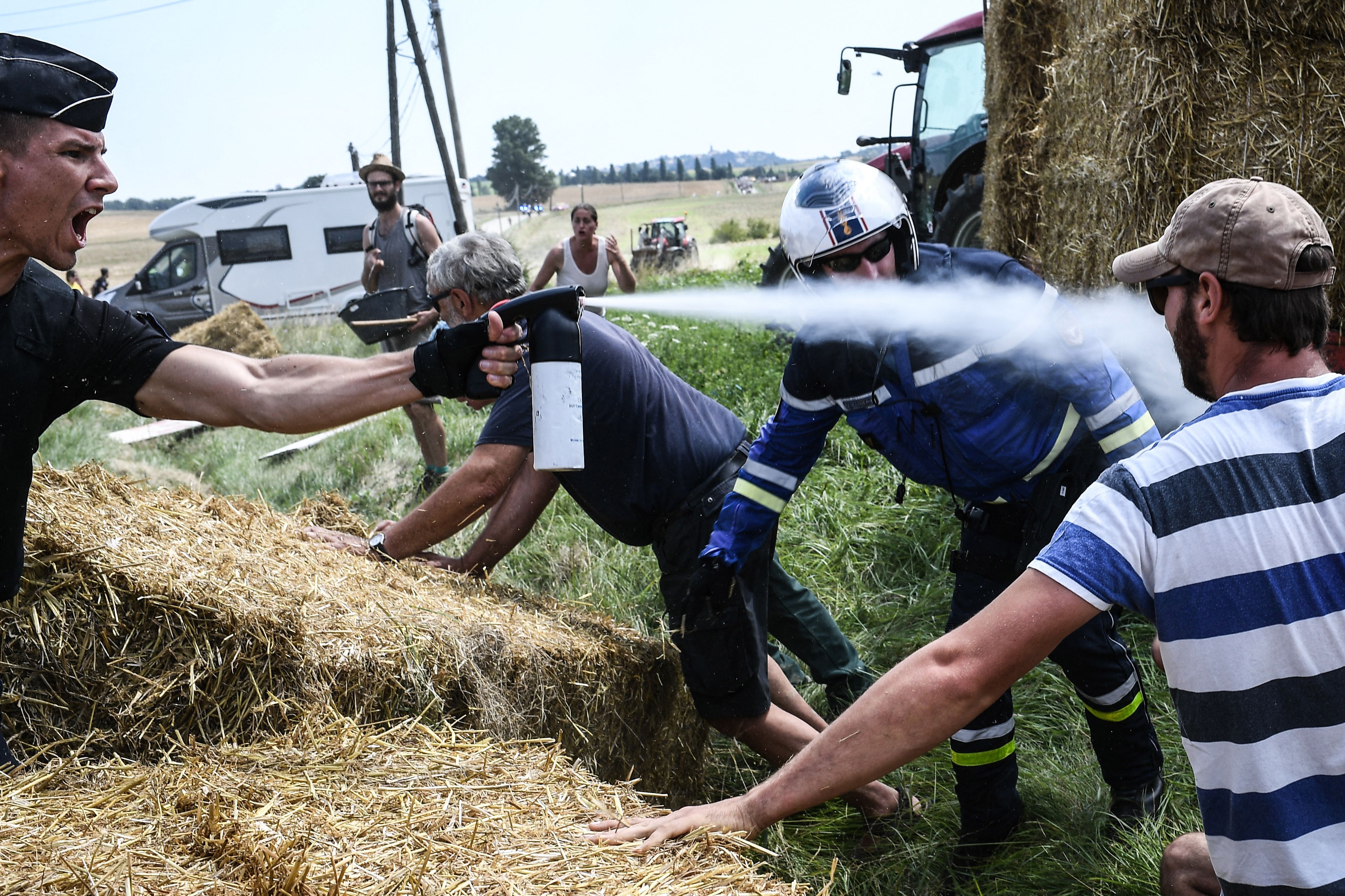 A gendarme sprays pepper spray at a protesting farmer at the Tour de France