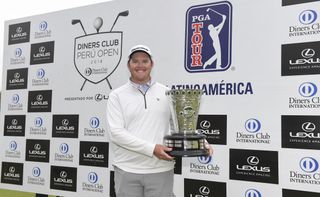 Higgs hold a trophy in front of a PGA Tour LatinoAmerica board