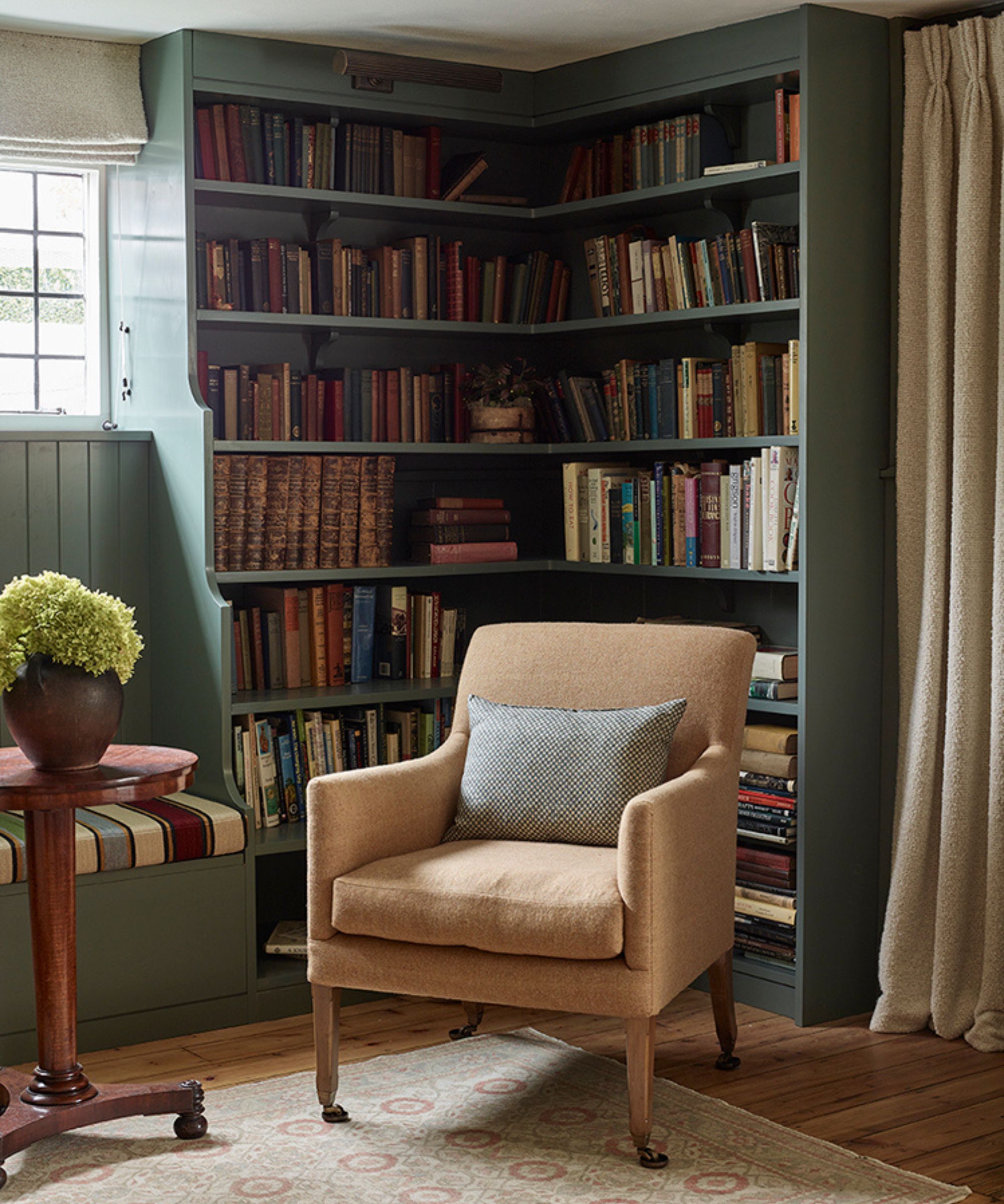 a library nook in a cottage in london painted dark green with a bench seat and arm chair